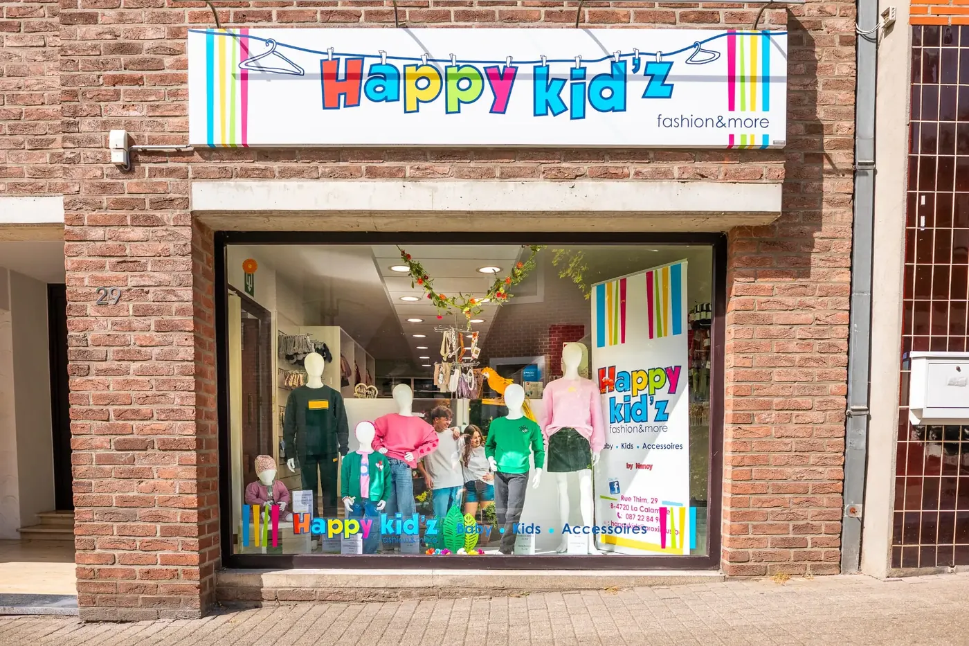 Vitrine de la boutique Happy Kid'z, décorée de mannequins habillés et de ballons colorés aux couleurs de la marque.